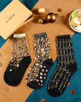 3 paires de chaussettes transparentes à paillettes dorées Atelier St Eustache posées à plat à côté du coffret de Noël doré dans une ambiance festive et lumineuse pour Noël