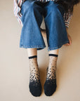Chaussettes transparentes à pois noirs, portées par une femme assise par terre et portant un jean bleu