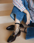 Chaussettes transparentes à pois noirs, portées par une femme assise par terre et portant un jean bleu avec des mocassins bordeaux