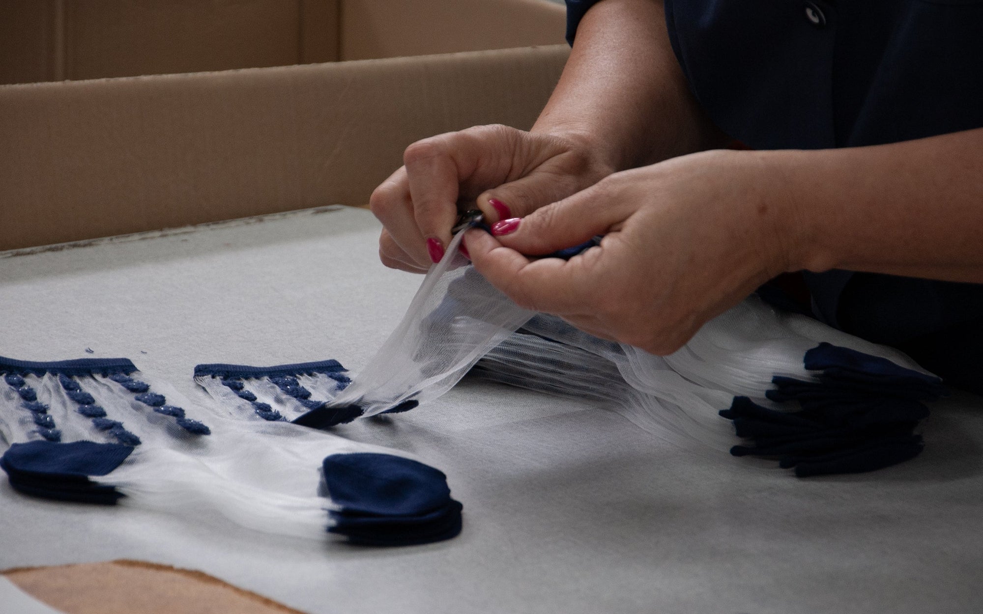 Gros plan sur les mains d’une femme en train de ranger une production de chaussettes transparentes aux motifs bleus.