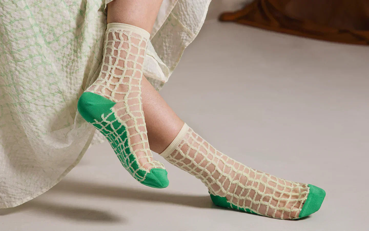 Zoom sur les pieds d’une femme portant des chaussettes transparentes à carreaux jaunes et verts sous les pieds.
