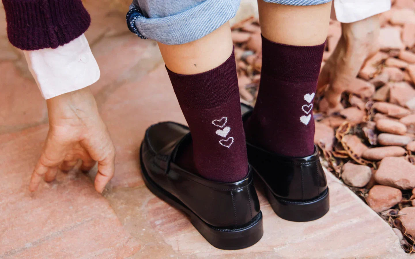 Zoom sur les pieds d’une mannequin portant des chaussettes en coton bordeaux, décorées de trois petits cœurs blancs alignés verticalement à l’arrière de chaque cheville.