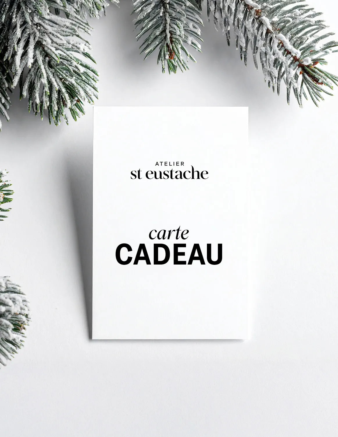 carte cadeau atelier st eustache posée à plat sur fond blanc avec des branches de sapin de noël