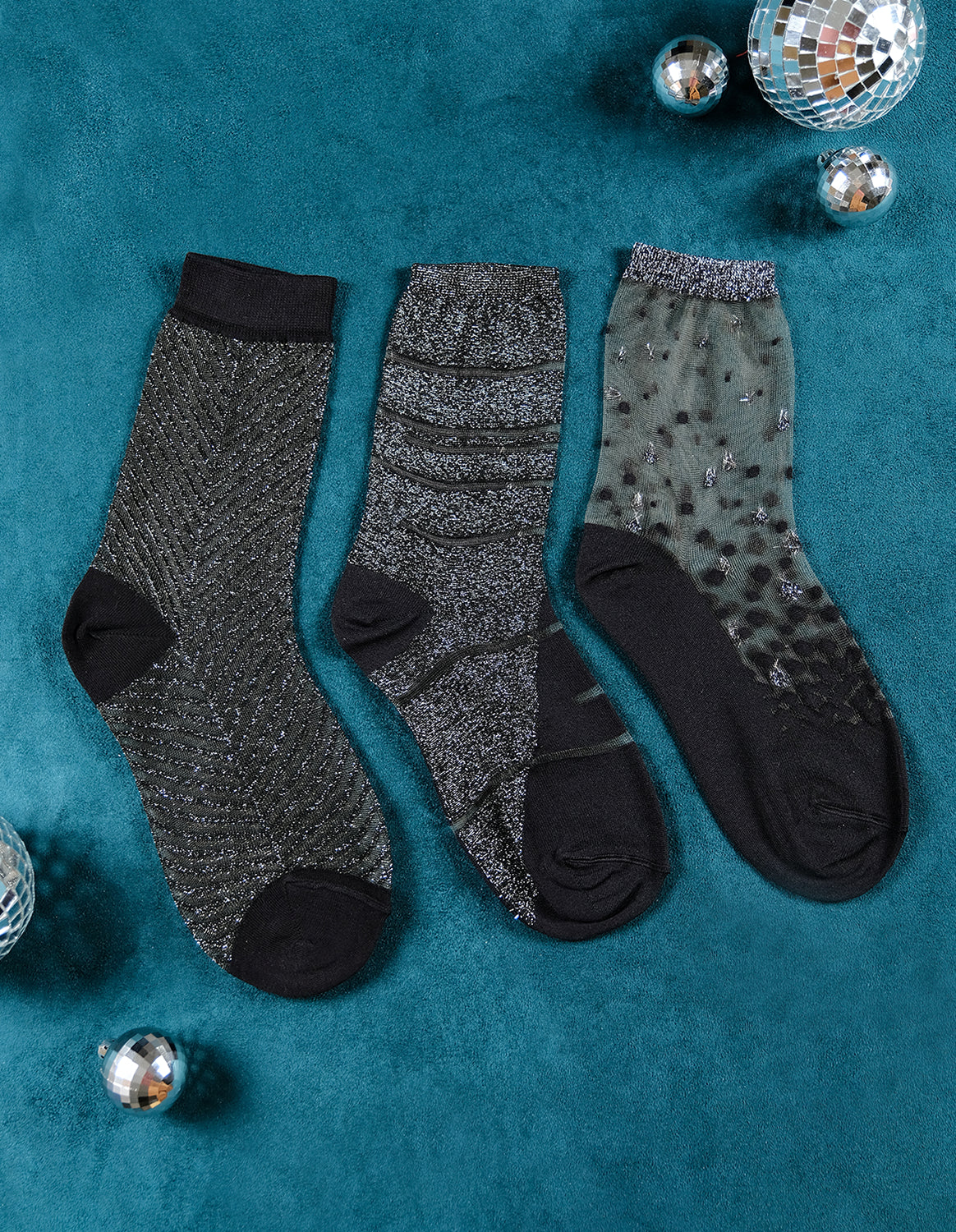 3 paires de chaussettes transparentes à paillettes argentées Atelier St Eustache posées à plat dans une ambiance hivernale pour Noël