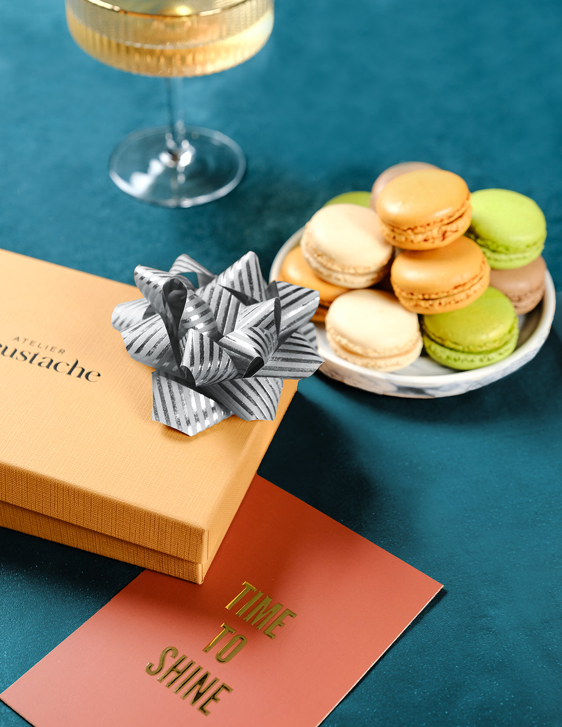 Coffret de Noël argenté Atelier St Eustache fermé avec un ruban cadeau disposé sur une carte cadeau dans une ambiance gourmande et festive