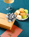 Coffret de Noël argenté Atelier St Eustache fermé avec un ruban cadeau disposé sur une carte cadeau dans une ambiance gourmande et festive