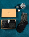 Coffret de Noël argenté Atelier St Eustache avec la paire de chaussettes transparentes à paillettes Nakameguro silver posée à plat et les modèles Sapin Silver et Tate Modern Silver pliés, dans une ambiance hivernale pour Noël