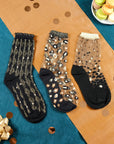 3 paires de chaussettes transparentes à paillettes dorées Atelier St Eustache posées à plat dans une ambiance festive et lumineuse pour Noël
