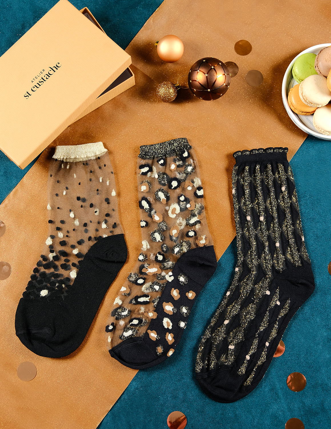 3 paires de chaussettes transparentes à paillettes dorées Atelier St Eustache posées à plat à côté du coffret de Noël doré dans une ambiance festive et lumineuse pour Noël