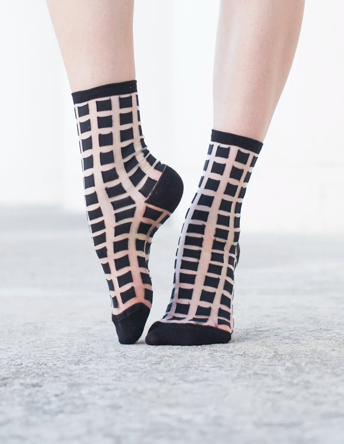 chaussettes transparentes à carreaux noirs pied pointé sur fond gris