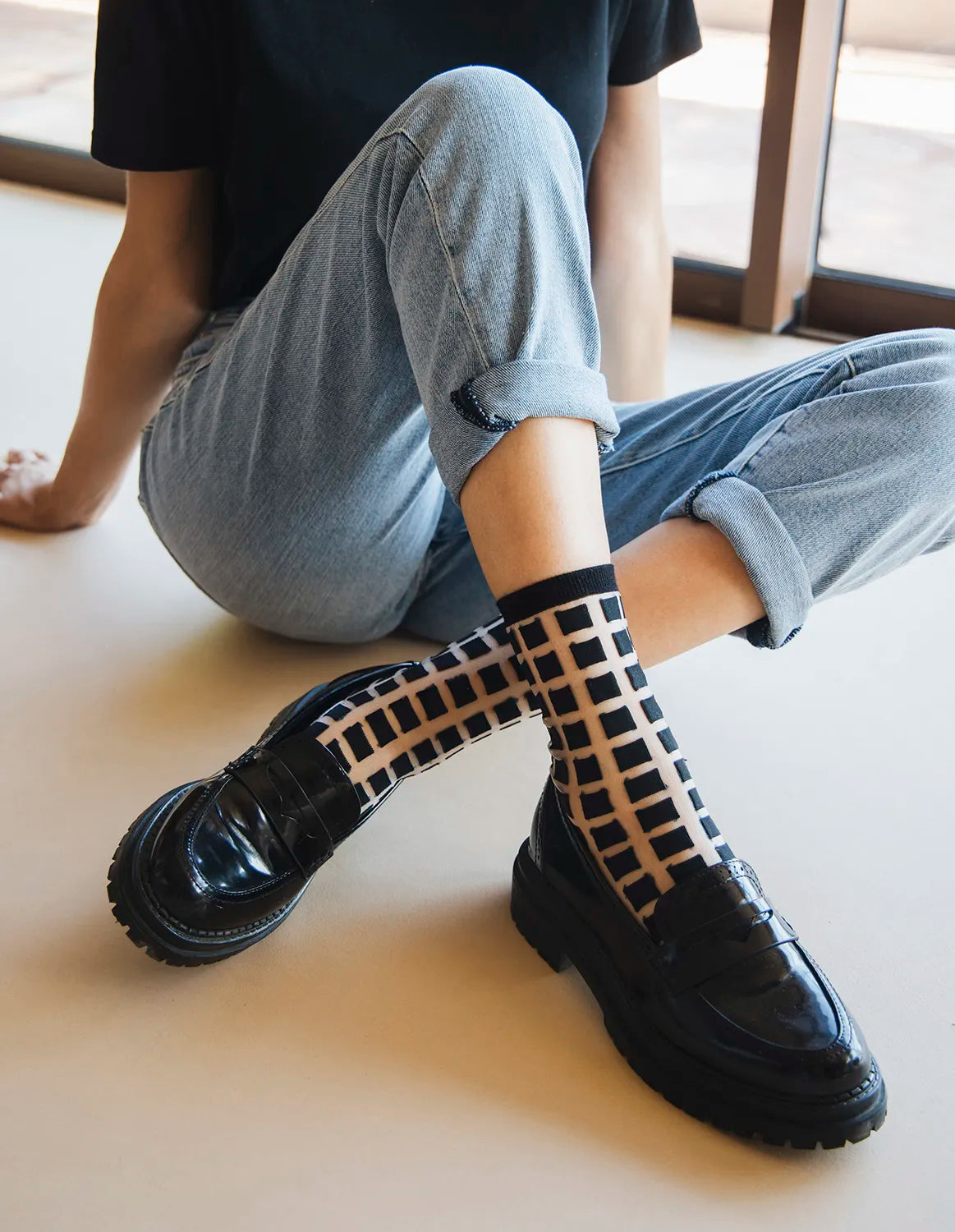 chaussettes transparentes à carreaux noirs et chaussures mocassins noirs jambes croisées jean bleu clair ambiance décontractée