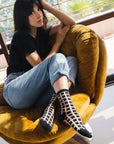 femme assise sur fauteuil jambes croisées avec chaussettes transparentes à carreaux noirs ambiance décontractée