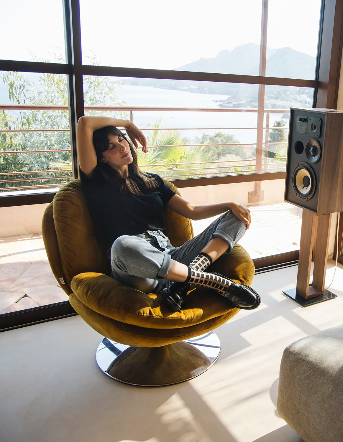 femme assise sur fauteuil dans une ambiance poétique avec paysage de mer en fond, tenue décontractée et chaussettes transparentes à carreaux noirs avec mocassins noirs