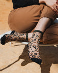Zoom de la paire de chaussettes transparentes léopard Horseshoe Bend Gold Atelier St Eustache portée par une mannequin assise avec un pantalon marron