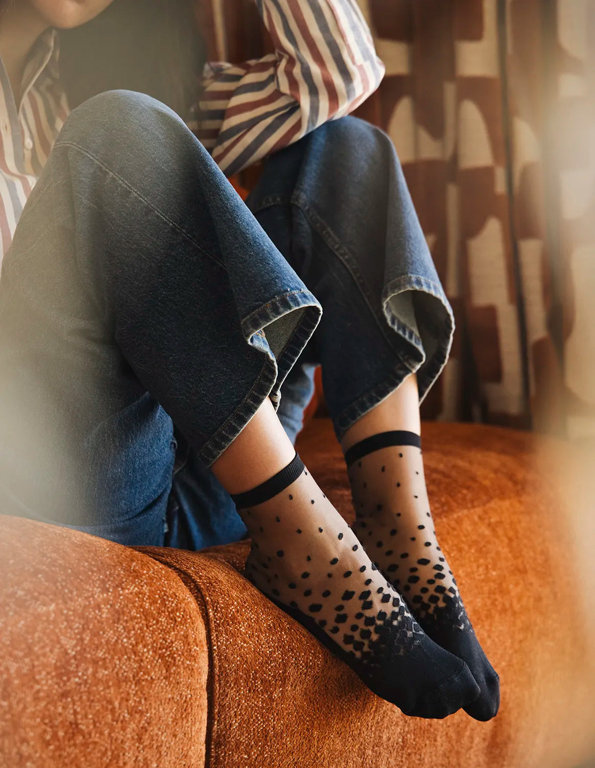 Chaussettes transparentes à pois noirs, portées par une femme assise sur un canapé cocooning en jean bleu