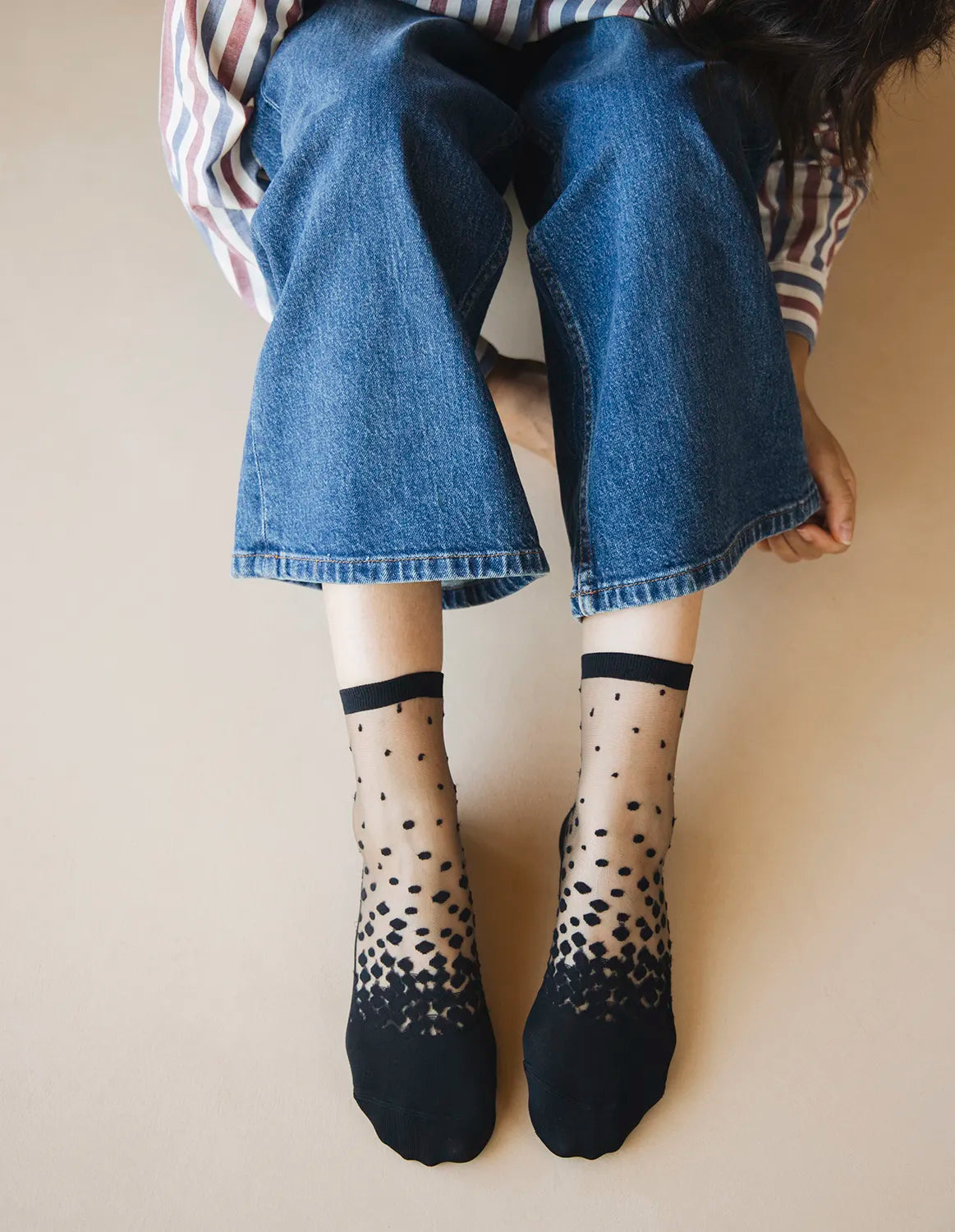 Chaussettes transparentes à pois noirs, portées par une femme assise par terre et portant un jean bleu