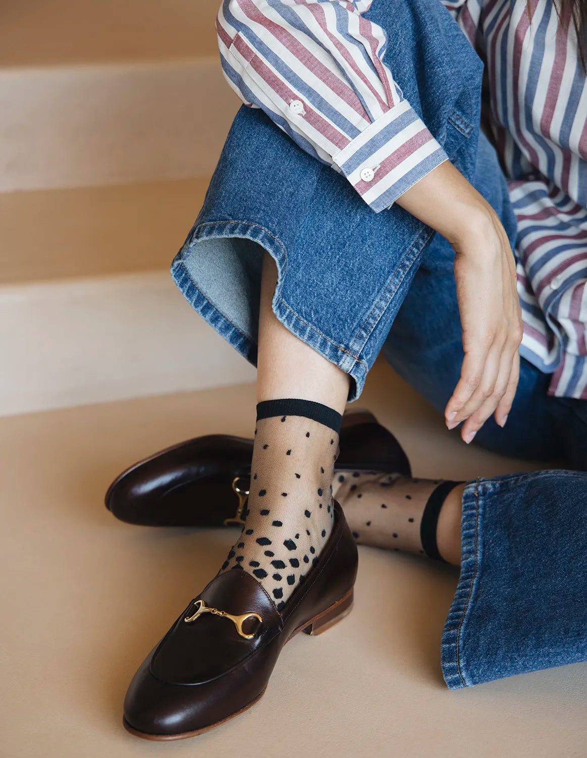 Chaussettes transparentes à pois noirs, portées par une femme assise par terre et portant un jean bleu avec des mocassins bordeaux