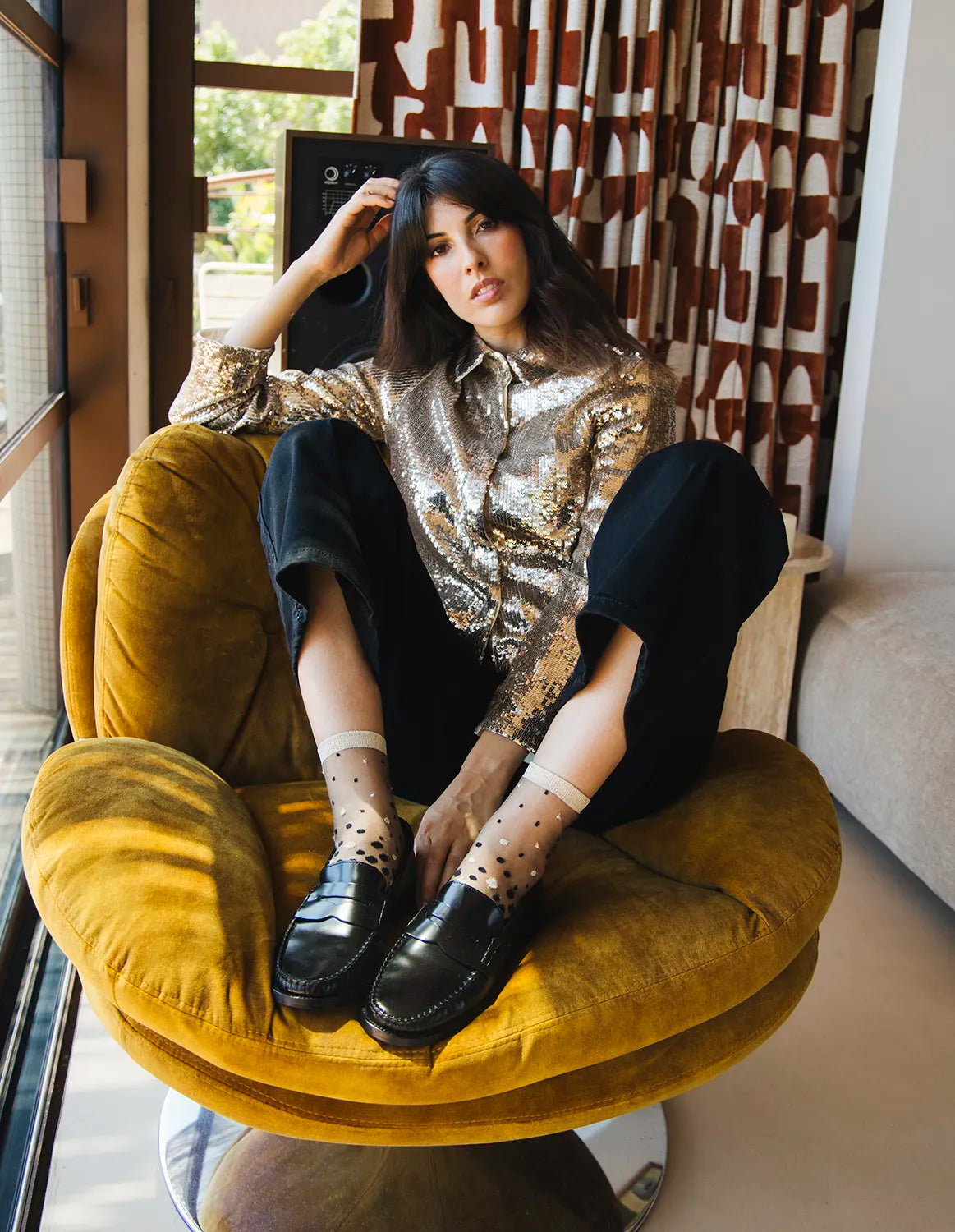 Paire de chaussettes transparentes à paillettes dorées Nakameguro Or Atelier St Eustache portée par une mannequin assise à la tenue festive à sequins dorés et aux mocassins brillants noirs