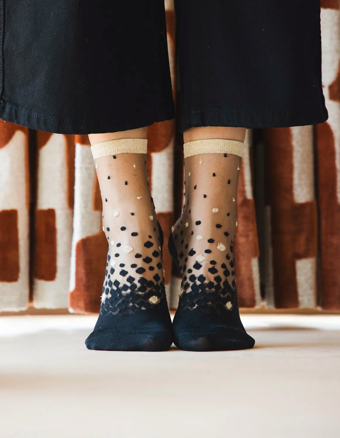 Zoom de la paire de chaussettes transparentes à paillettes dorées Nakameguro Or Atelier St Eustache portée par une mannequin sur les pointes avec un pantalon noir